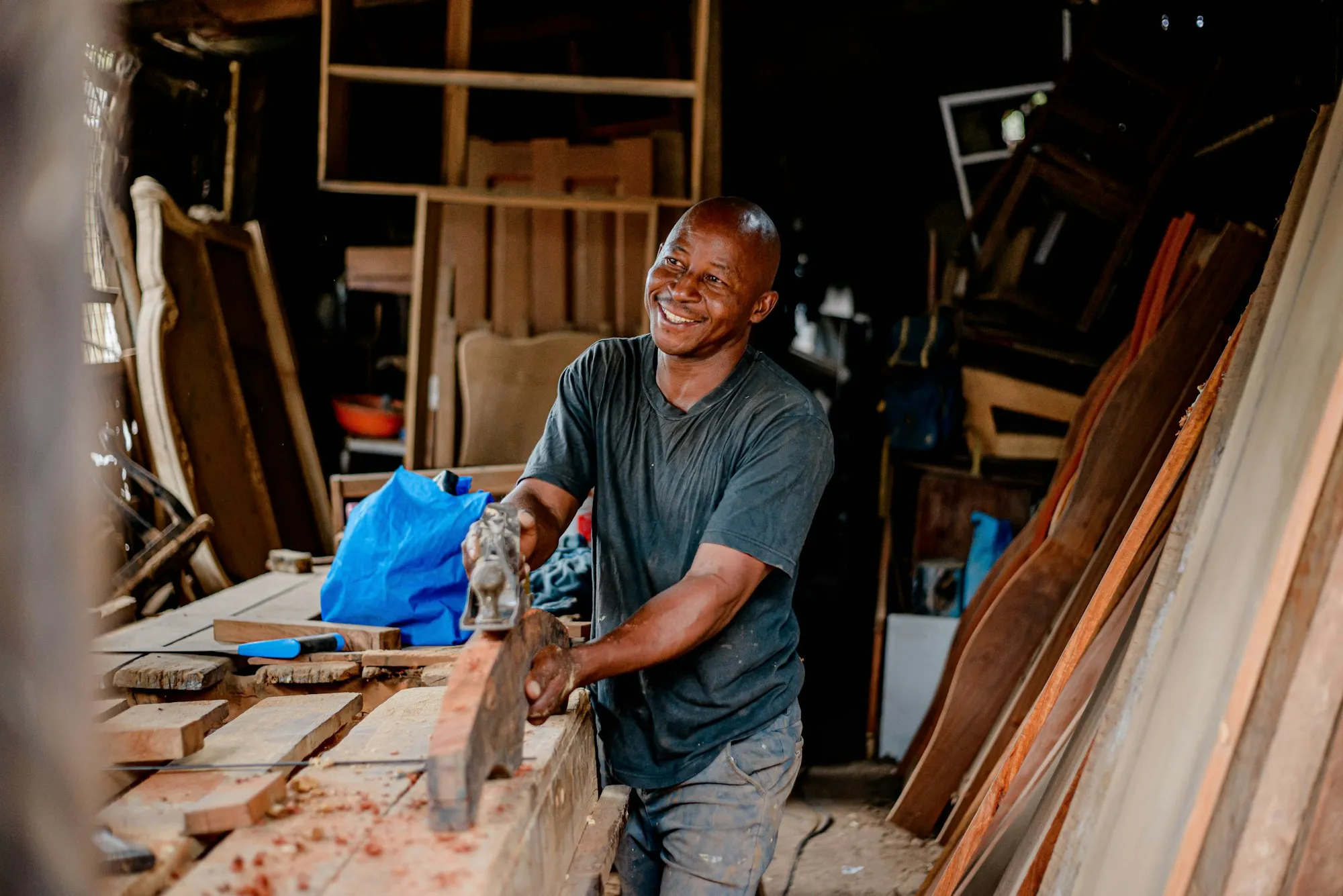 A furniture maker smiling at his workbench, surrounded by timber.